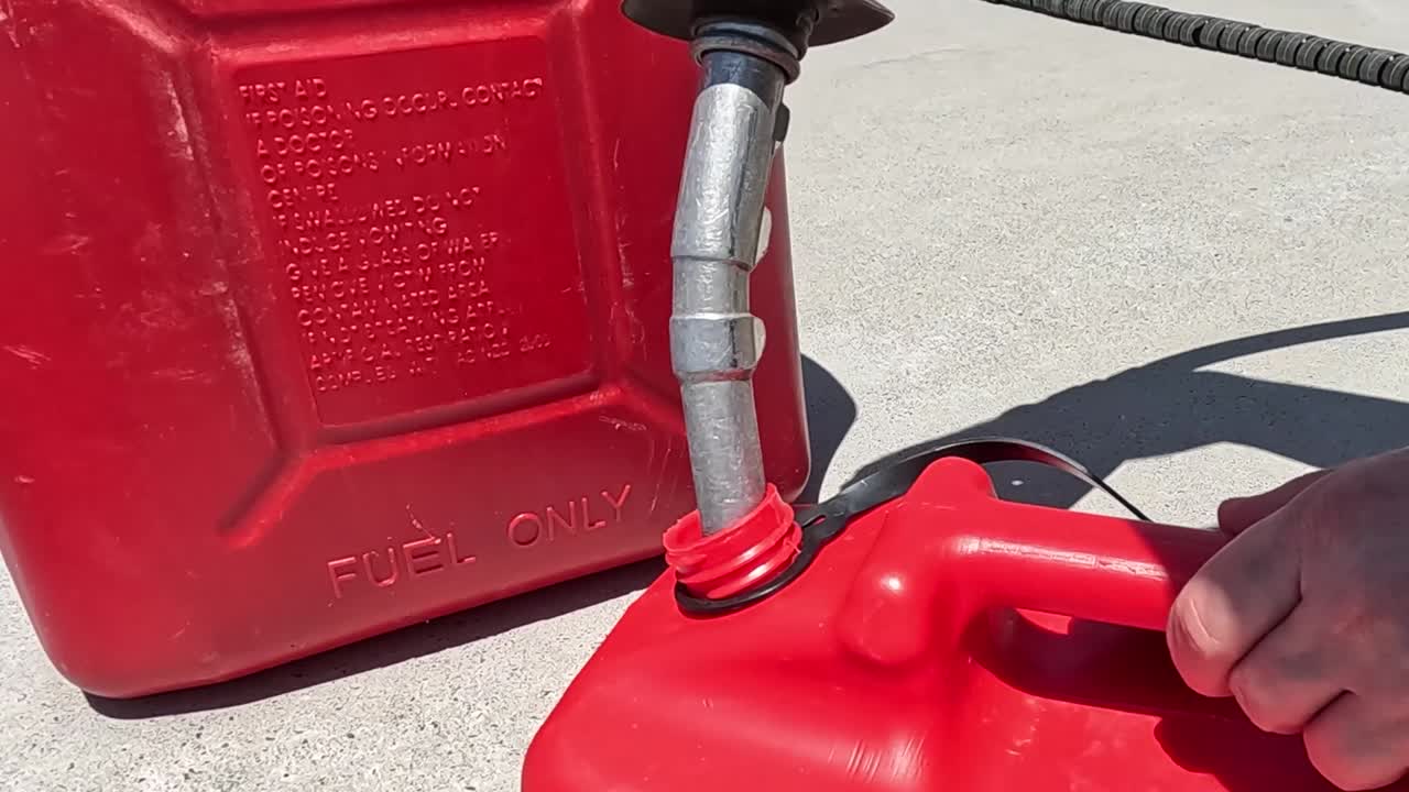 Close-up of fuel spilling from a red container while refueling outdoors in sunlight.