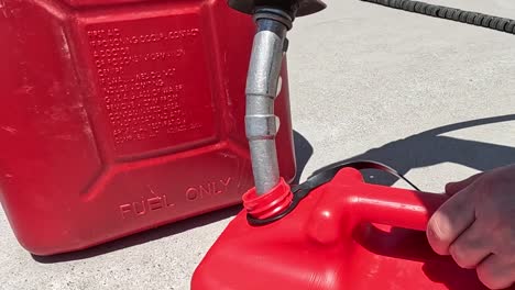 close-up of fuel spilling from a red container while refueling outdoors in sunlight.