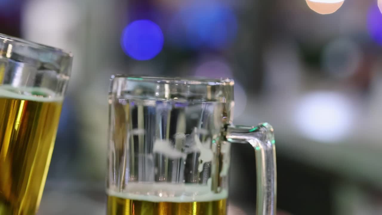 dos personas haciendo sonar vasos de cerveza en un entorno nocturno borroso