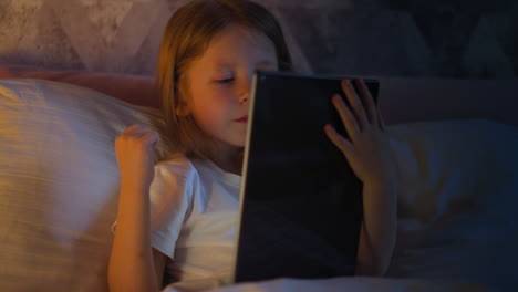 niño alegre feliz de ganar en el videojuego en la tableta en la cama