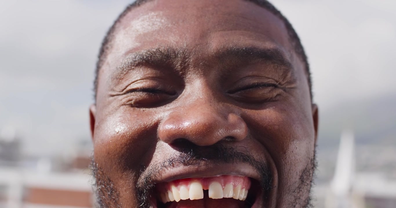 Uomo afroamericano di mezza età che sorride, rivelando uno spazio tra i denti, mentre la telecamera inizia un primo piano su un tetto.