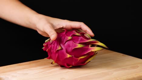 hand places dragon fruit on wooden table