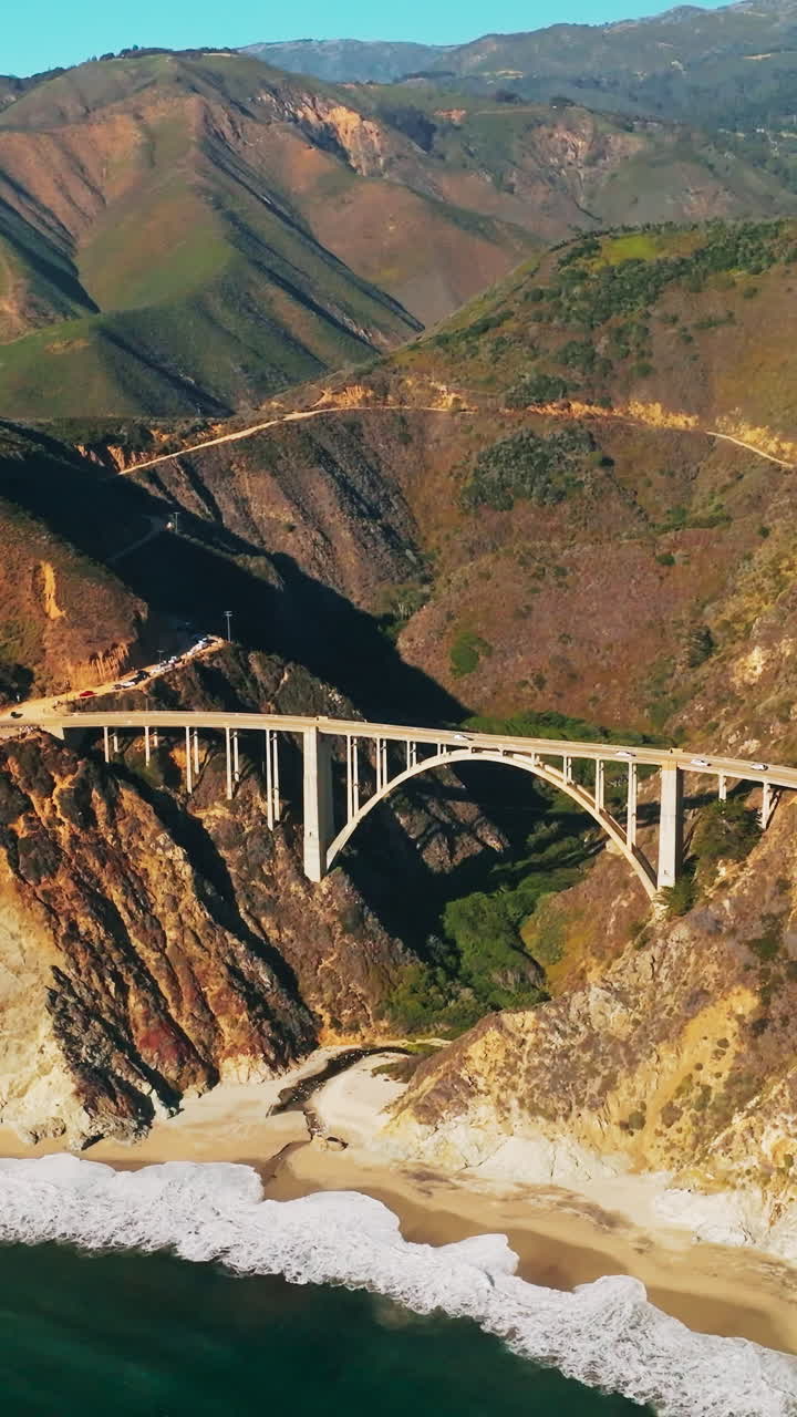 Splendid panorama of California mountains with bridge at the foot. Little sandy beach with white waves slowly arriving to. Aerial view. Vertical video