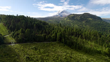 Disparo-De-Dron-Hacia-Atrás-Tipo-Dronie-Que-Muestra-La-Cima-Nevada-Del-Volcán-Popocatepetl-En-La-Ciudad-De-México-Y-Los-Frondosos-Bosques-Que-Lo-Rodean