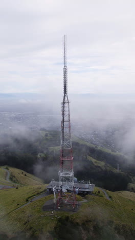 vertical drone shot orbiting the sugarloaf mountain tower in foggy new zealand