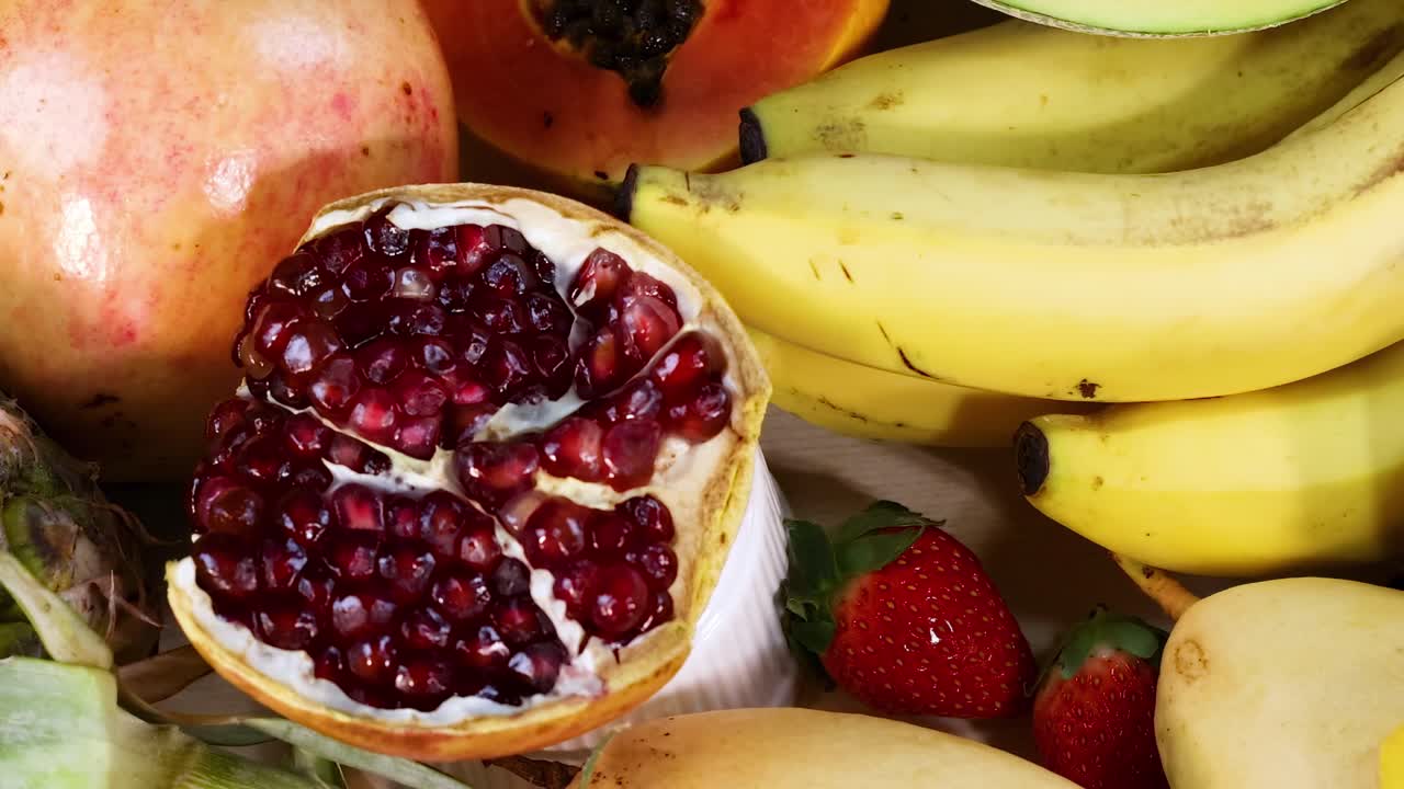 A colorful arrangement featuring bananas, kiwi slices, oranges, and pomegranate on a vibrant backdrop.