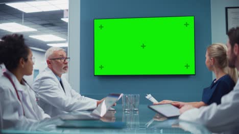sala de conferencias del hospital con un equipo diverso de médicos que miran la pantalla verde de chroma key y hablan. expertos médicos en atención médica desarrollan nuevos medicamentos, medicamentos, métodos de tratamiento del paciente