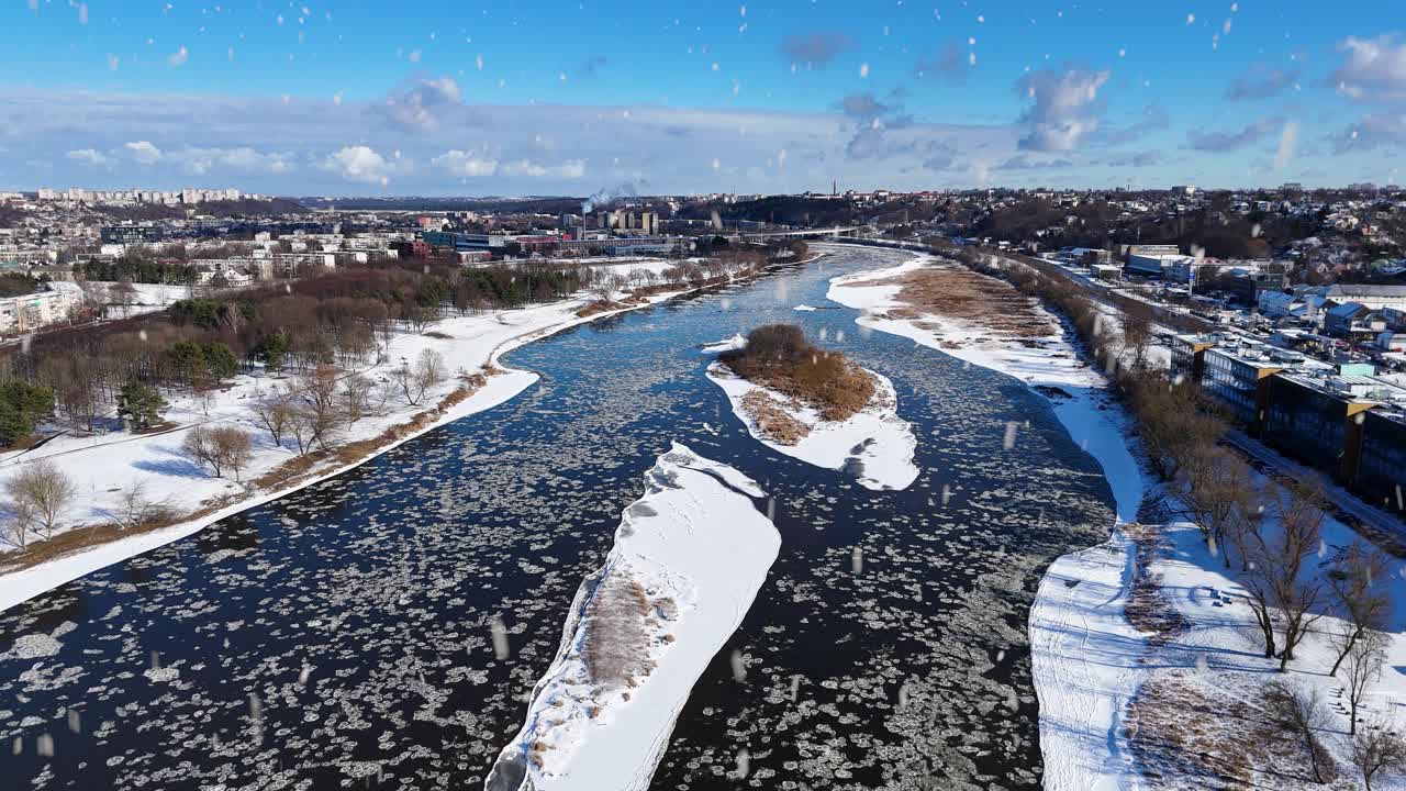 Snowfall over icy Neris River and Kaunas city, aerial view