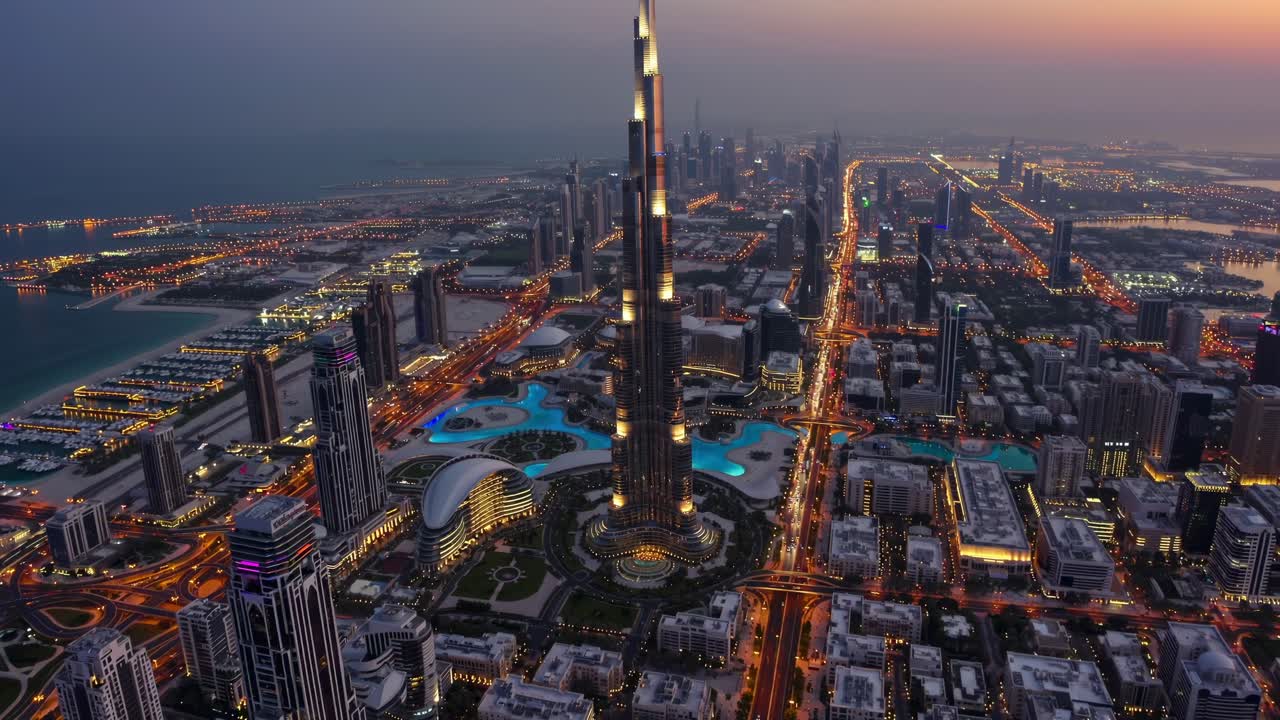 Urban skyline glowing during twilight, featuring prominent skyscraper rising above illuminated streets, surrounding architectural structures, metropolitan infrastructure