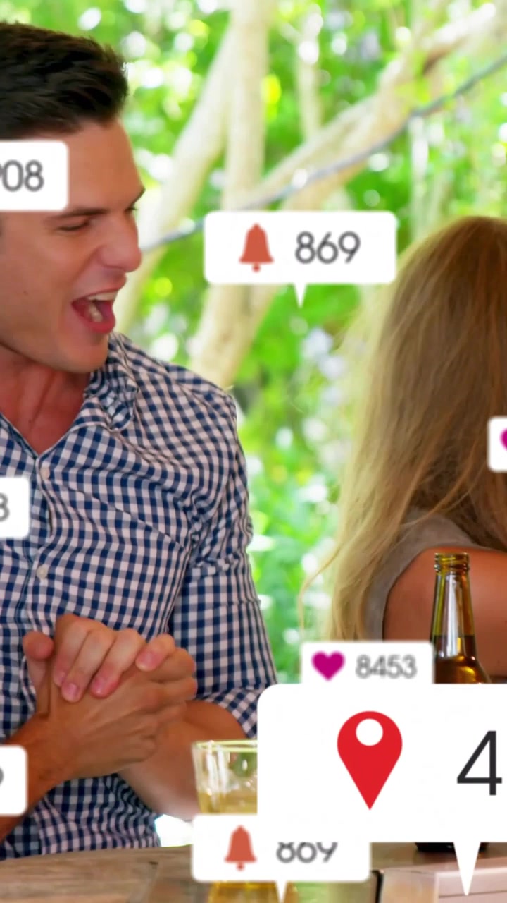 Video verticale: Coppia di amici che reagiscono a badge social che si aggiornano e si accumulano sopra un tavolo in un patio.