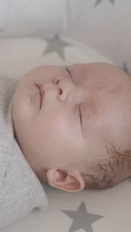 cute infant son wrapped in muslin swaddle sleeps tired after massage lying in small baby bed close view