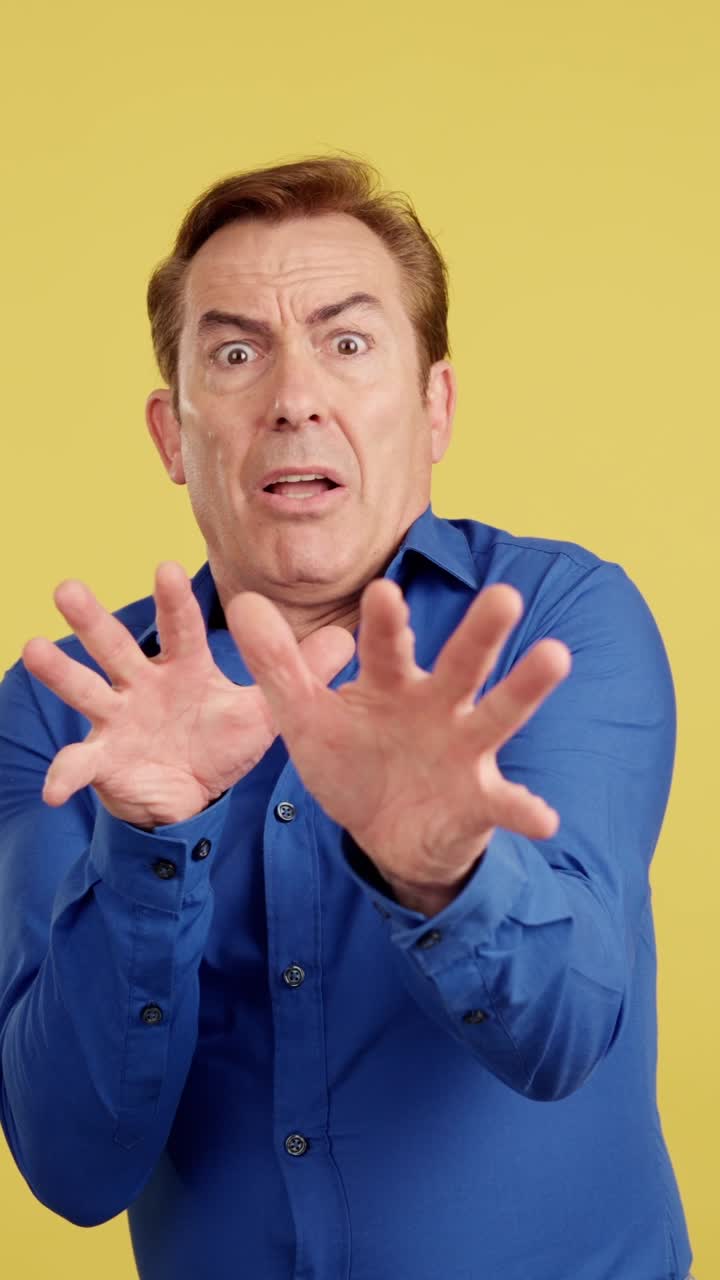 Man reacting with shock or fear, hands raised on yellow background