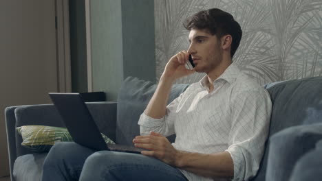 Confident-man-using-laptop-phone-same-time.-Guy-working-with-smartphone-computer