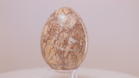 Large-fragmented-Granite-egg-rotating-slowly-on-a-turntable-in-front-of-a-white-background