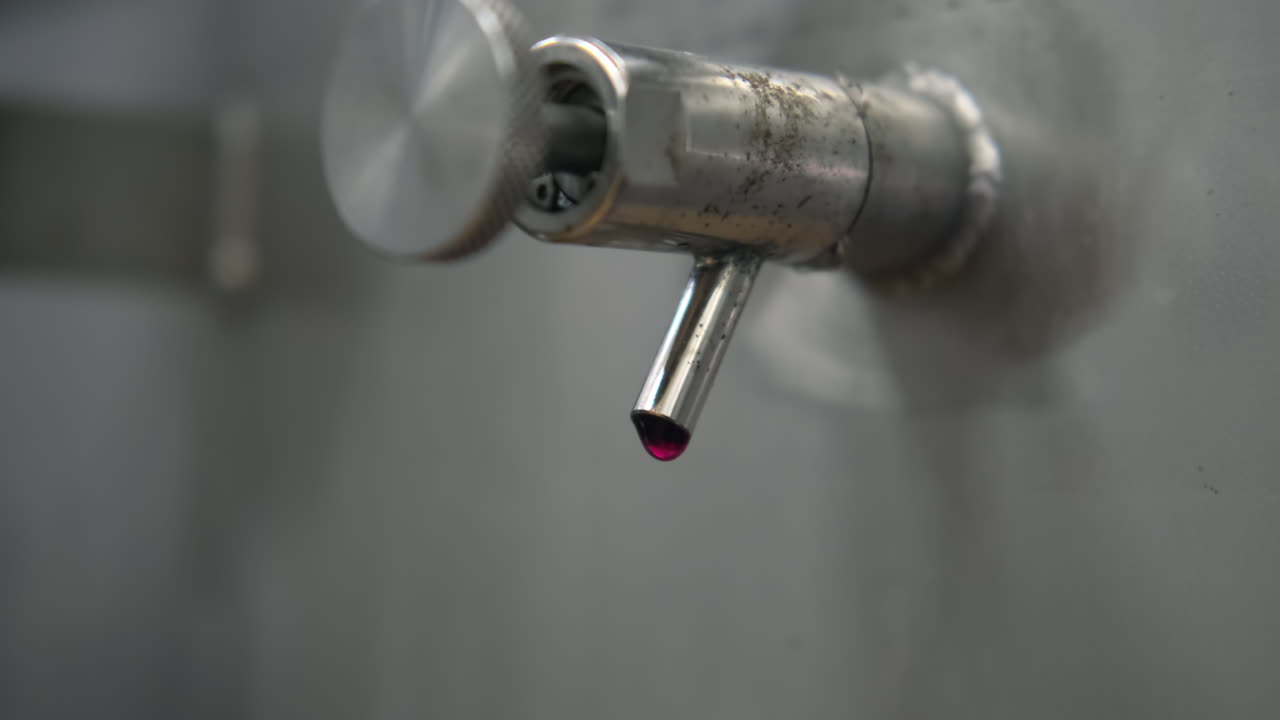 grifo de metal industrial con goteo de líquido rojo