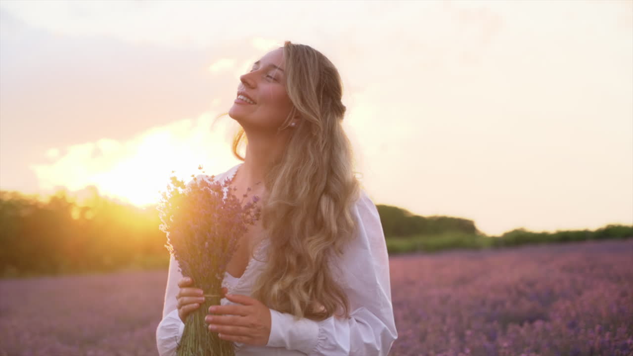 Woman in a white dress holding a bouquet of lavender in a field at sunset