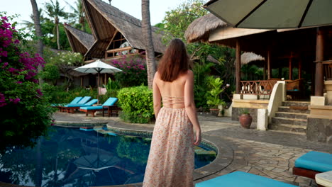 woman walking through a tropical resort with a swimming pool and lush gardens