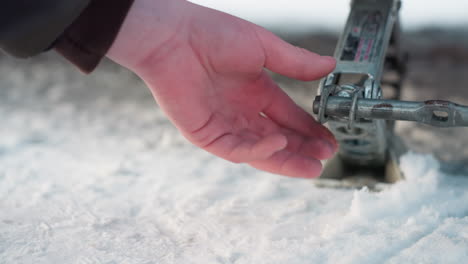 close up of metal rod engaged in jack lifting on snow covered ground, hand turning bar to raise vehicle support, shiny silver mechanism reflecting cold light during outdoor winter repair activity