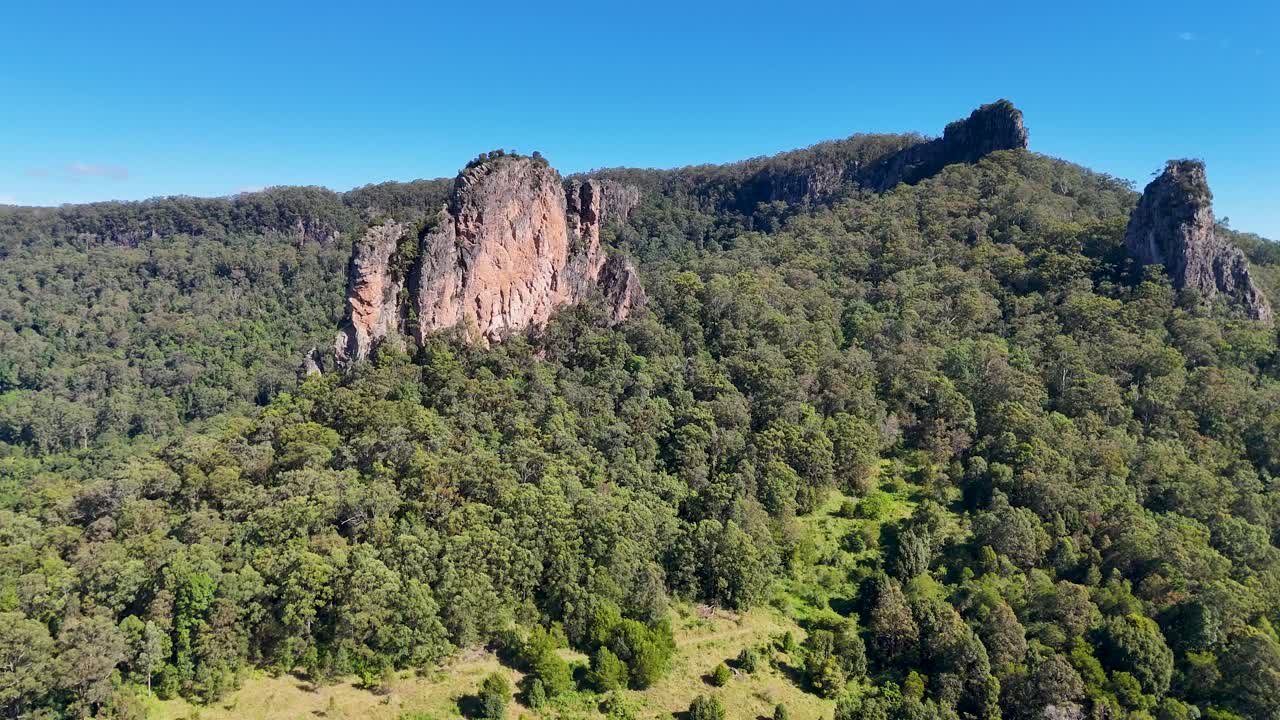 Drone footage captures the lush greenery and striking rhyolite formations of Nimbin Rocks under clear blue skies