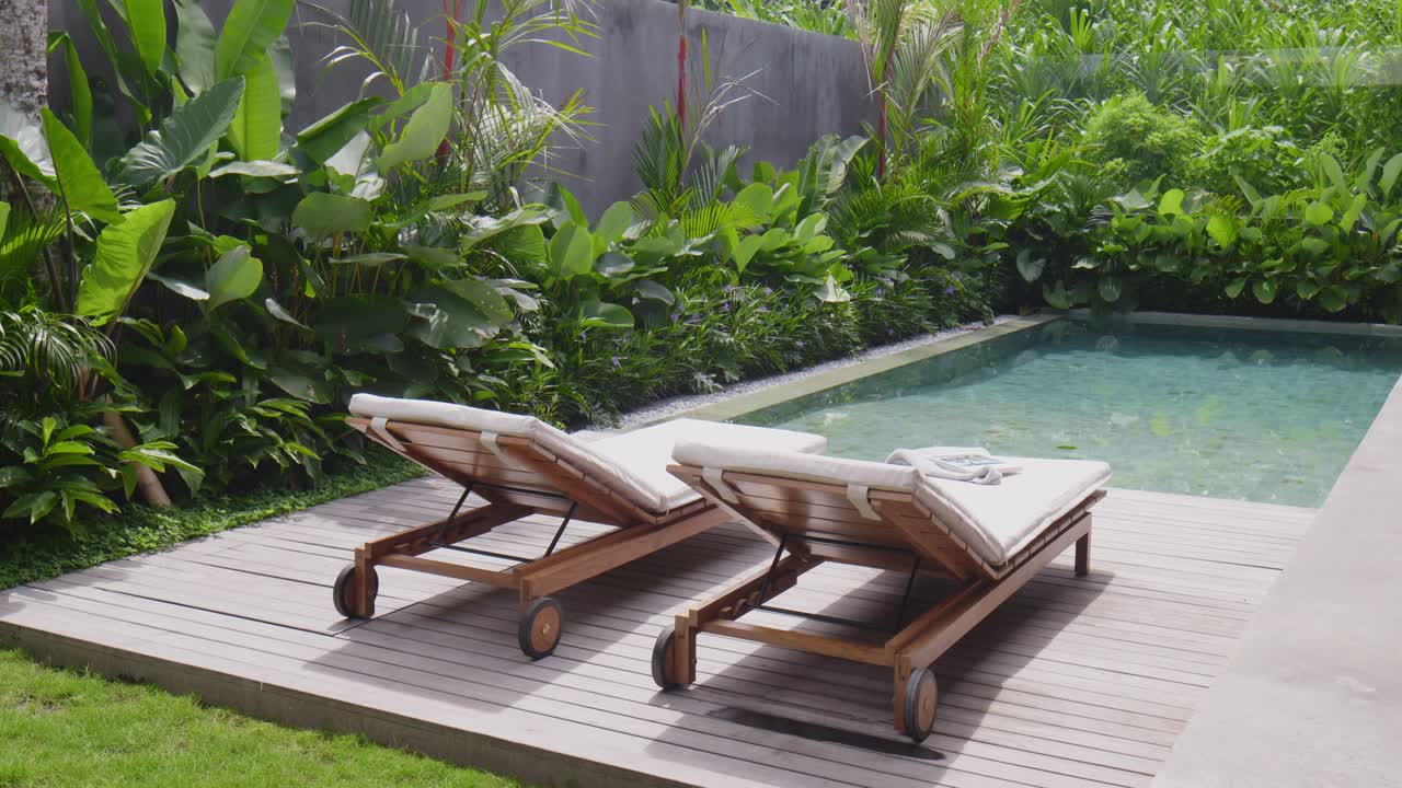 Relaxing poolside chairs by a green tropical garden in sunny weather