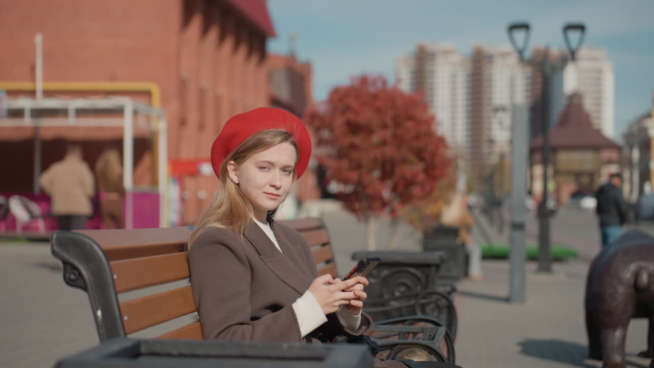 Signora di città sicura di sé. Donna elegante con cappello rosso. Donna urbana alla moda con un sorriso radioso nel paesaggio cittadino. Donna sicura di sé con un berretto rosso chic che scatta una foto in mezzo al trambusto della città.