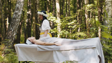 therapist female doctor making woman relaxing spa face massage with hands outdoors in the forest