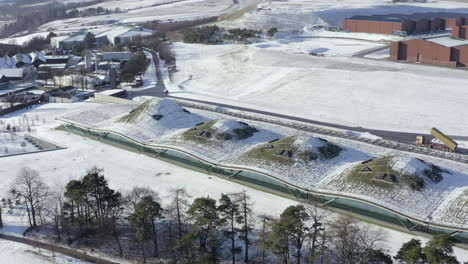 Aerial-view-of-the-Macallan-whisky-distillery-surrounded-by-snow-on-a-sunny-winters-day,-Moray,-Scotland---advancing-shot---rising-right-to-left