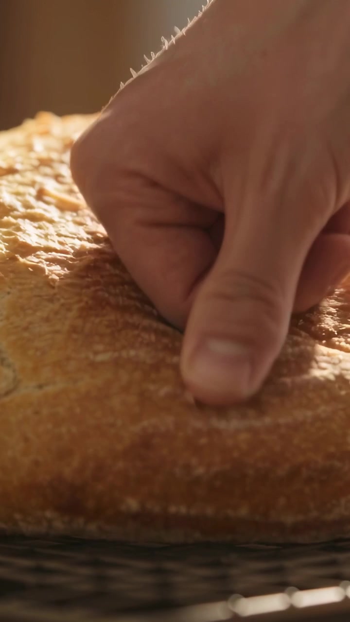 Vertical video: Pressing adult hand entering, probing loaf on rack at counter, checking doneness