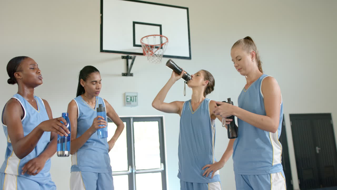 Drinking water, female basketball players taking break during practice in gym
