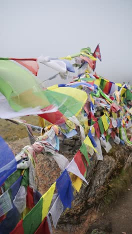 vertical buddhist prayer flags close up in misty mountains in nepal, vertical video for social media instagram reels and tiktok of tibetan prayer flags in mist in the himalayas blowing in the wind
