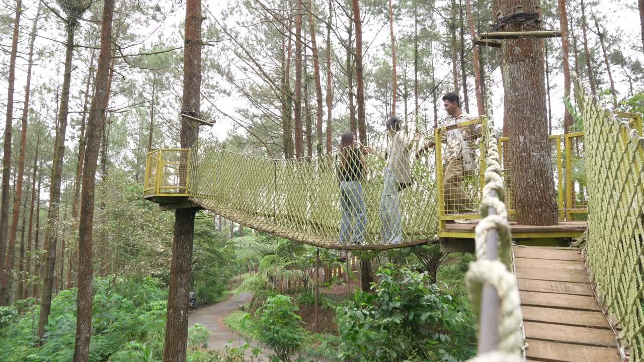 Young Asian Friends Crossing Rope Bridge in Forest Adventure