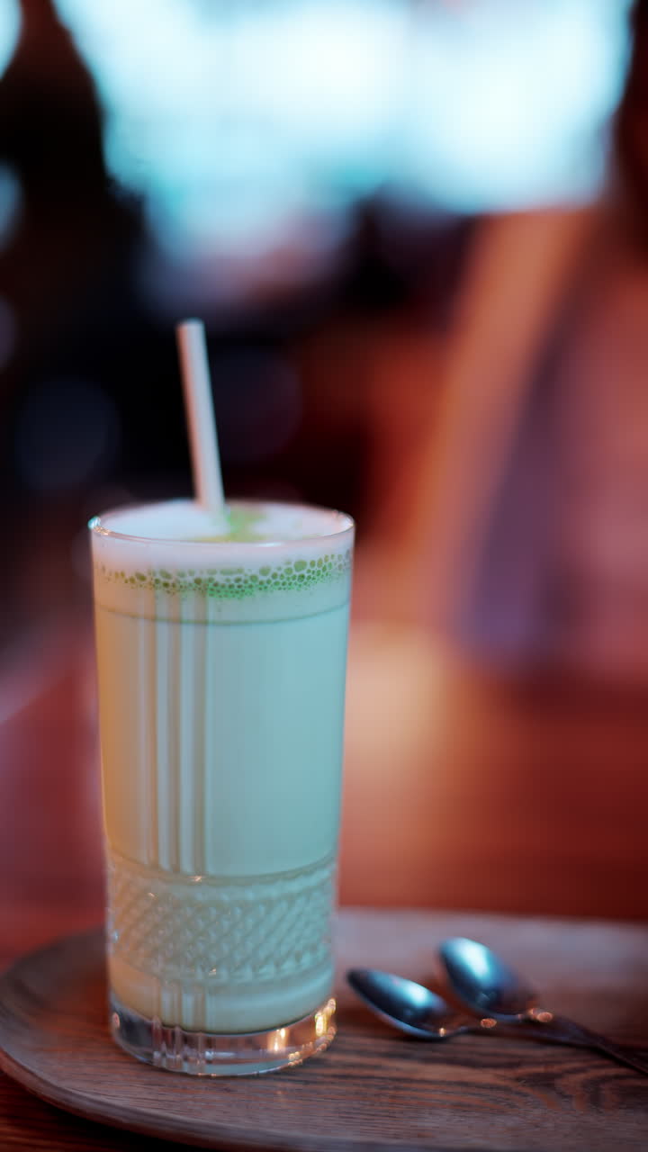 Close up of a matcha latte in a glass with a straw on a table at a cafe. Vertical