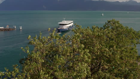 Jib-up-over-green-trees-revealing-a-ferry-moving-over-beautiful-lake-Geneva