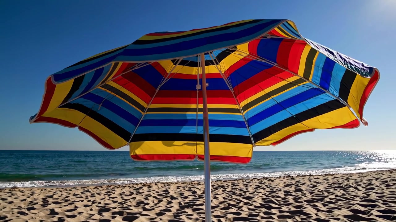 Ombrellone da spiaggia a strisce colorate su una spiaggia sabbiosa e soleggiata
