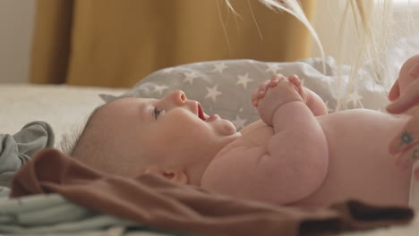 Closeup-of-baby's-hands,-upper-body,-mothers-blond-hair,-newborn-in-playful-mood-dressing-white-bedroom