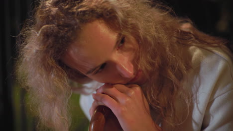 close up of young student with curly hair wearing white coat looking to side with thoughtful expression under soft night lighting, background slightly blurred with glowing bokeh