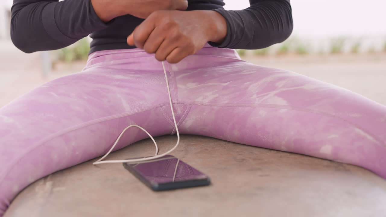 Donna rilassata che indossa cuffie all'aperto. Donna in abiti casual con auricolari che si prende una pausa all'aperto. Donna atletica rilassata vestita con leggings rosa e abbigliamento casual che si gode il tempo libero all'aperto.