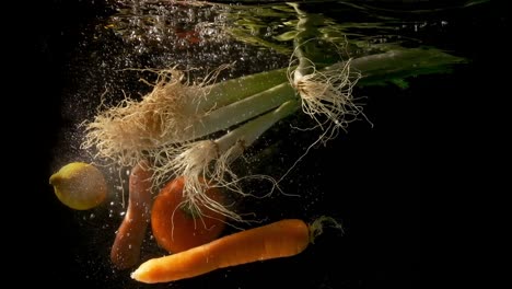 green onions, tomato, carrots and lemon falling together in the clear and dark water