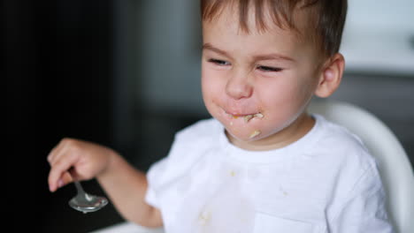 lovely cute toddler having lunch from spoon. mom's hand cleans the kid's mouth with napkin. close up. blurred backdrop.