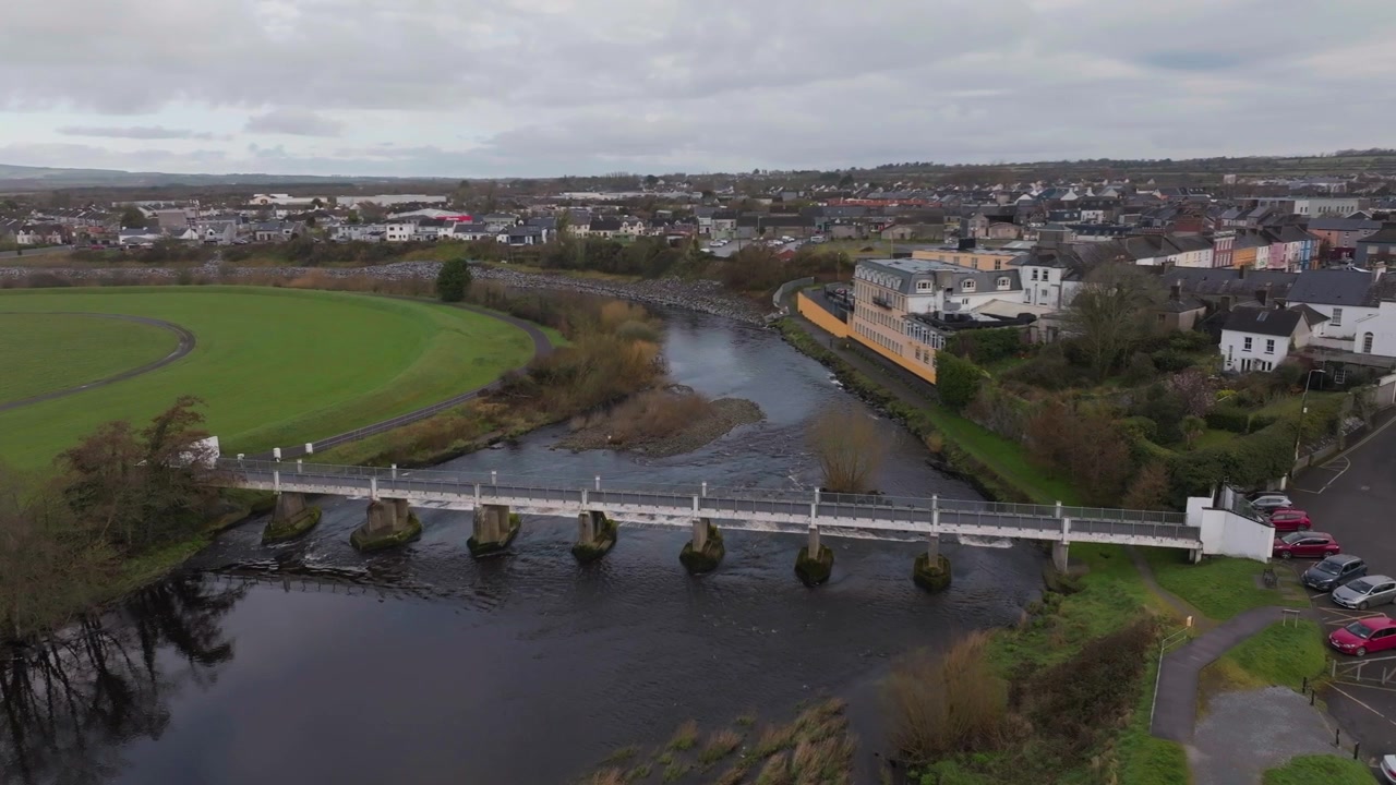 Et filmatisk luftfoto av en gangbro i stein som krysser elven Feale i Listowel, County Kerry. Viser irsk byarkitektur og bærekraftig byplanlegging