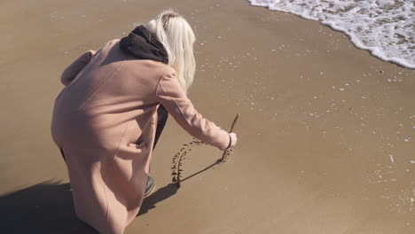 une femme dessine une forme de coeur dans le sable au bord de la mer alors que la vague de l'océan l'emporte