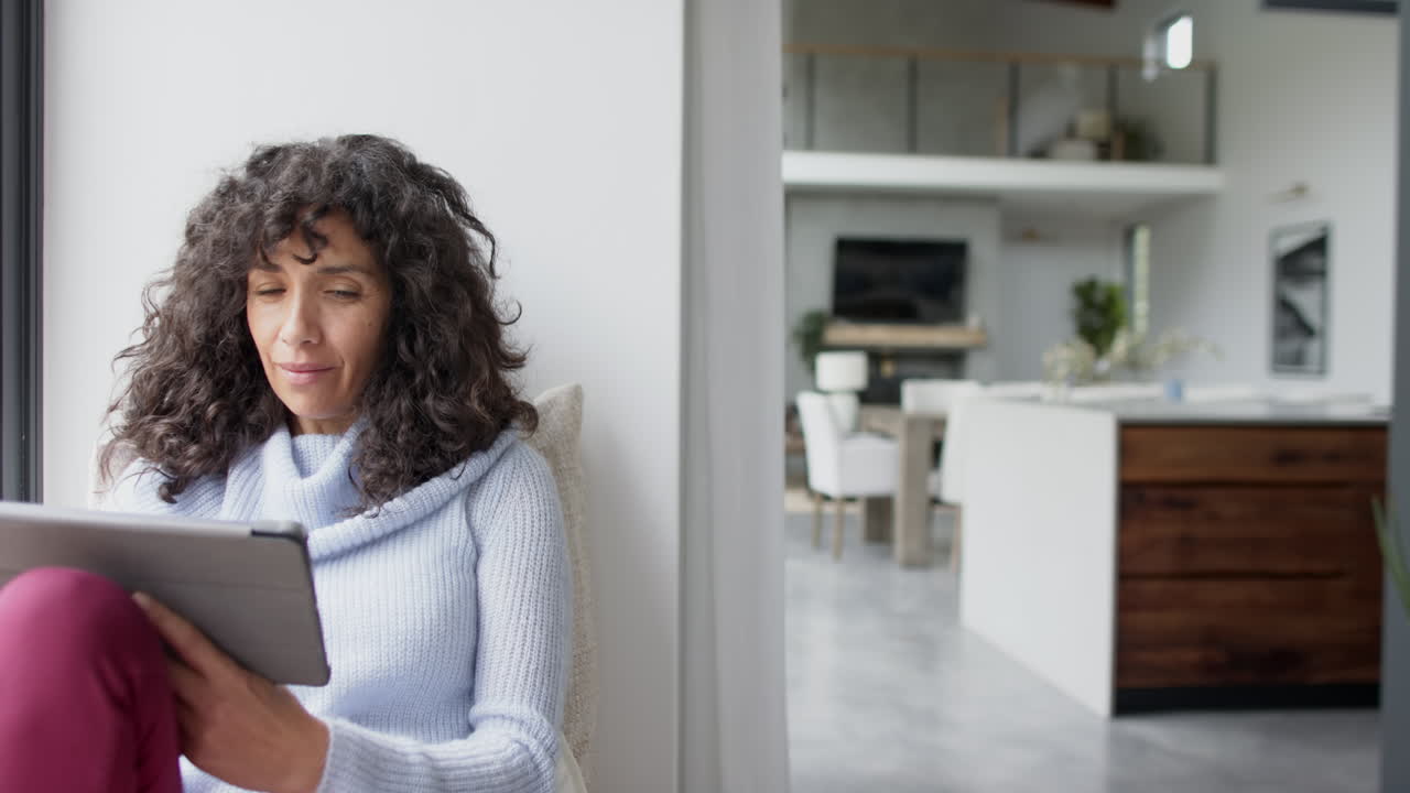 feliz mujer caucásica madura sentada en la ventana y usando la tableta en casa, cámara lenta