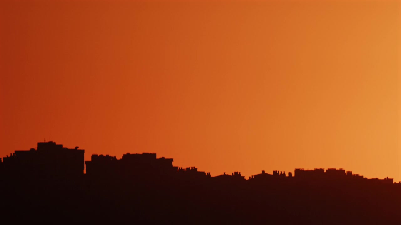 Silueta de un horizonte urbano contra un cielo de atardecer naranja intenso