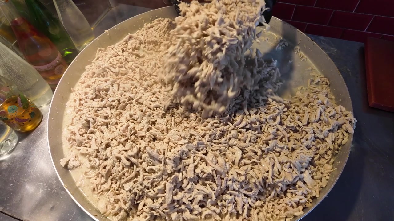 Chef che mescola pollo sfilacciato in una padella capiente