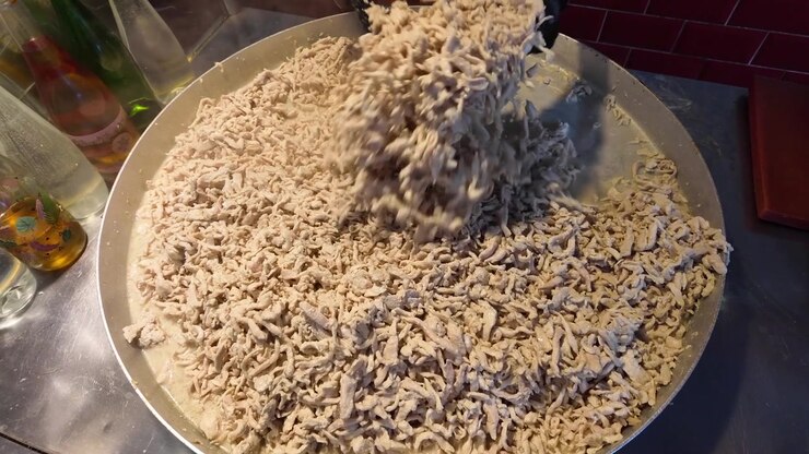 Koch mischt zerkleinertes Hähnchen in großer Pfanne