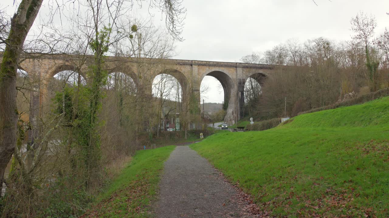 antiguo viaducto que se eleva sobre la exuberante vegetación en un día nublado en normandía, francia, con un camino de grava
