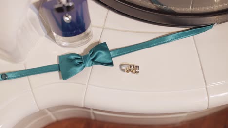 Wedding-rings-rolling-on-the-white-floor-near-green-groom's-bow-tie-and-perfume