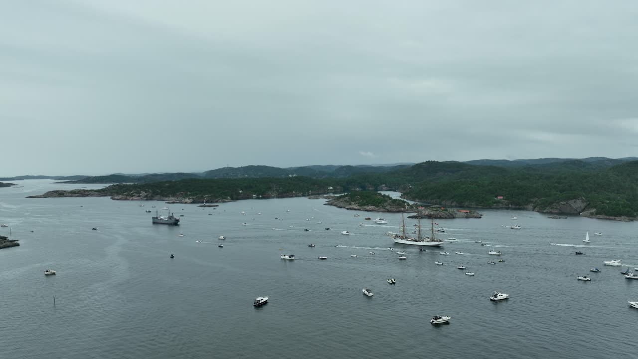 Numerous boats are anchored in the tranquil waters of a coastal area, surrounded by lush hills under a cloudy sky just before evening. The scene evokes a peaceful maritime atmosphere