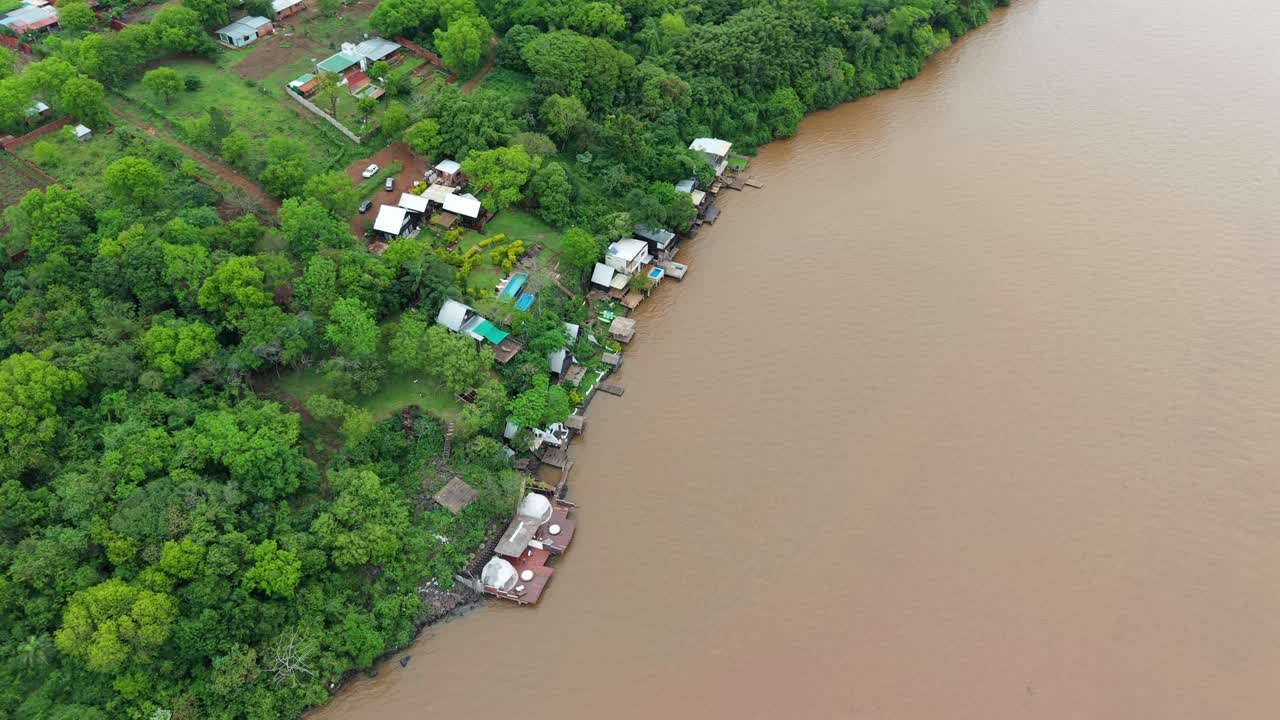 Rural riverside houses surrounded by lush green forest on the Paraná River captured from above, Puerto Lagier, Misiones, Argentina