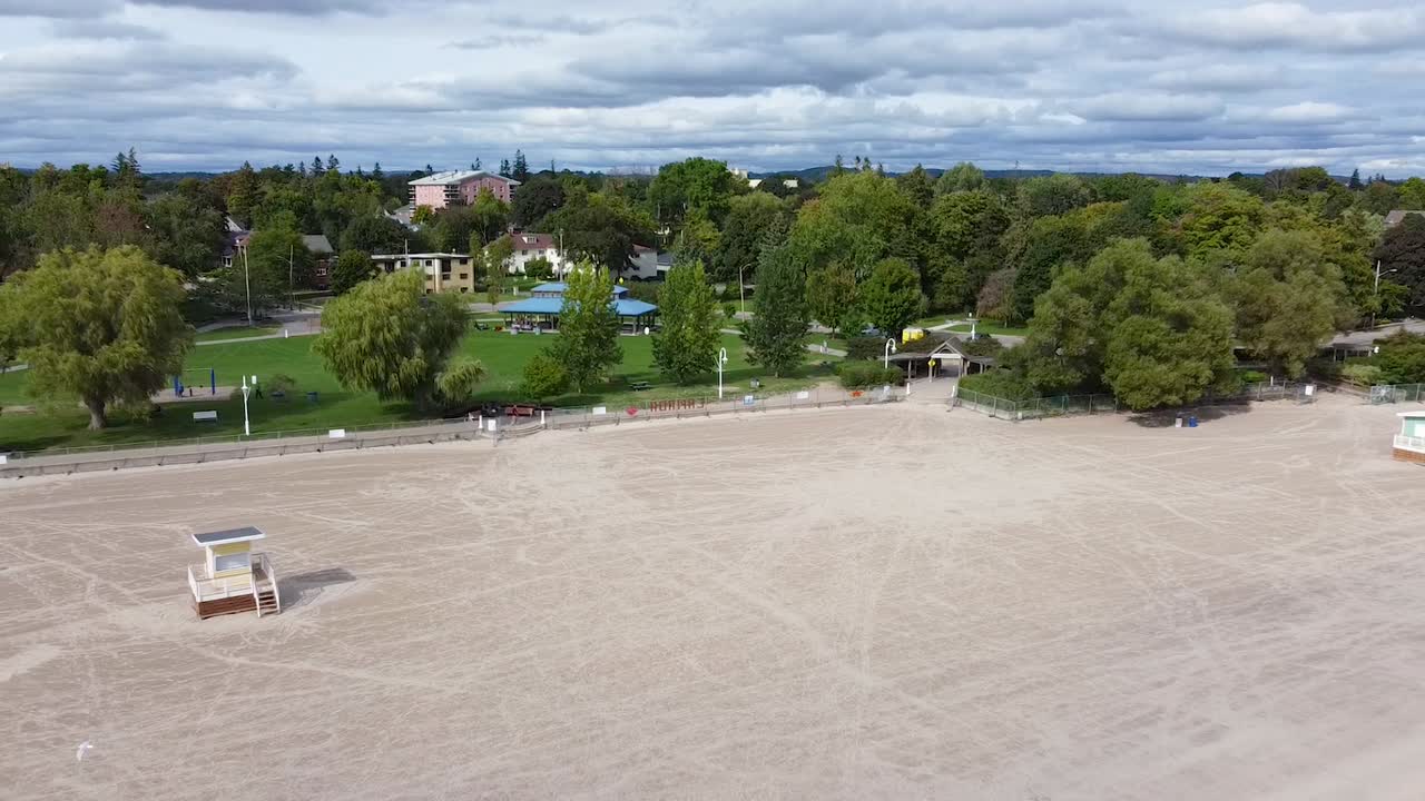 playa de arena blanca limpia y vacía con cabañas de salvavidas, paseo marítimo y parque arbolado en la ciudad turística